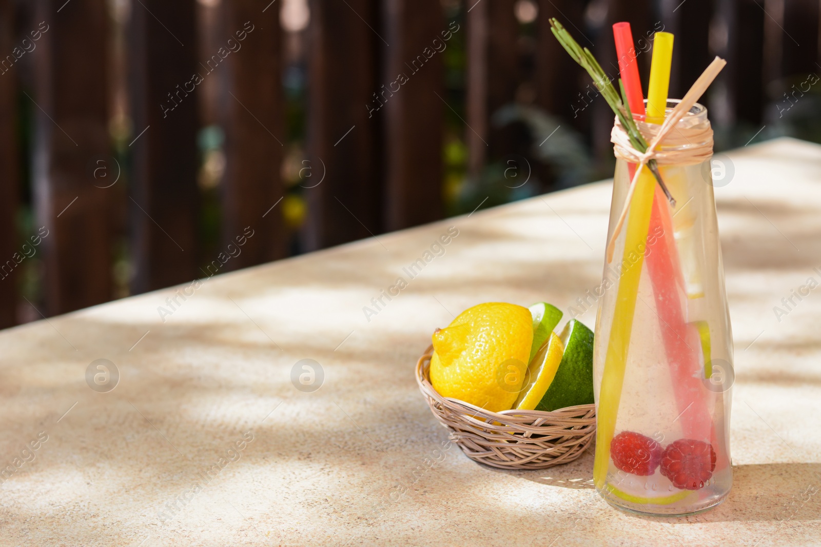 Photo of Refreshing tasty lemonade served in glass bottle and citrus fruits on beige table. Space for text