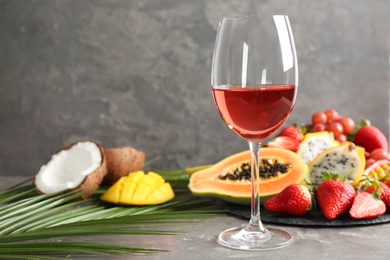 Delicious exotic fruits and glass of wine on grey table, space for text