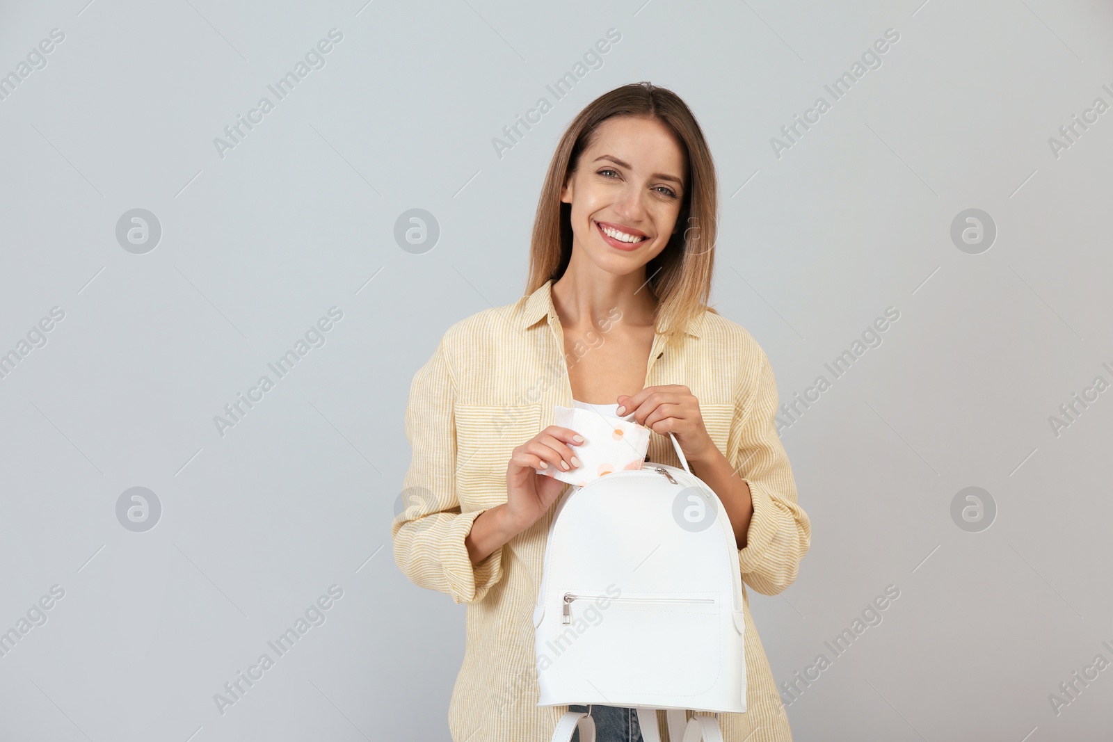 Photo of Happy young woman putting disposable menstrual pad into backpack on grey background