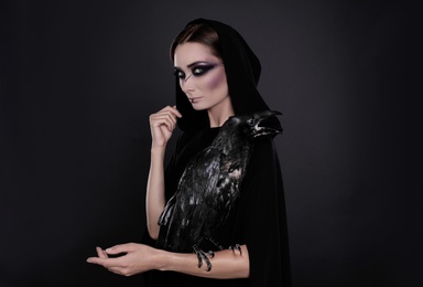 Photo of Mysterious witch with raven on black background