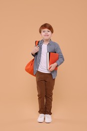 Photo of Cute schoolboy with backpack and books on beige background
