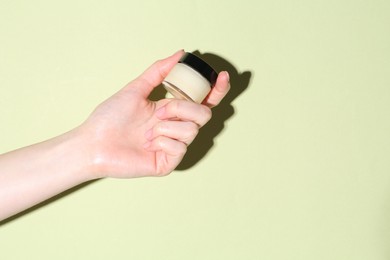 Woman holding jar of cream on green background, closeup. Space for text