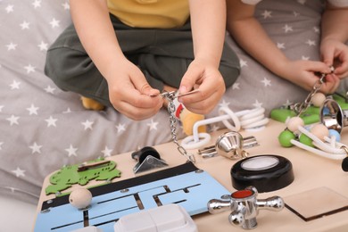 Photo of Little children playing with busy board on bed, closeup