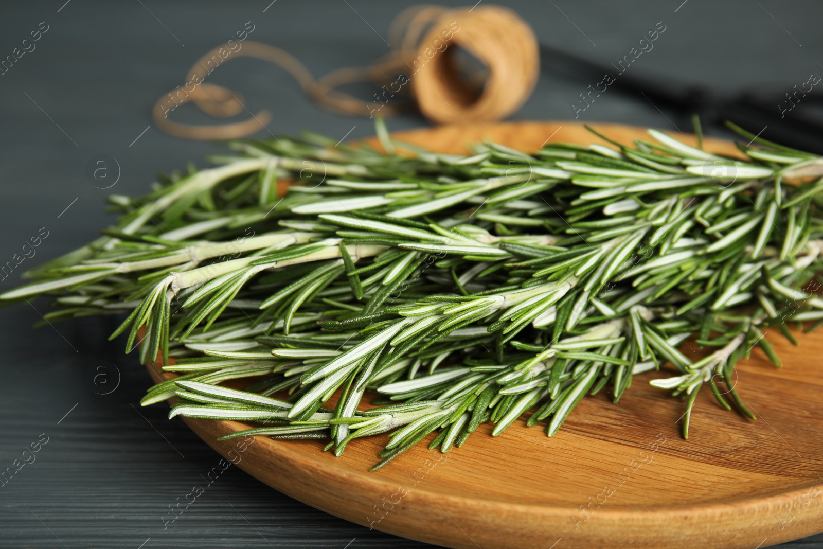 Photo of Wooden plate with fresh rosemary twigs on table, closeup