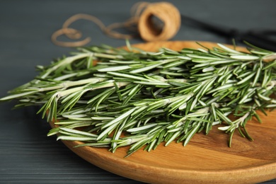 Wooden plate with fresh rosemary twigs on table, closeup