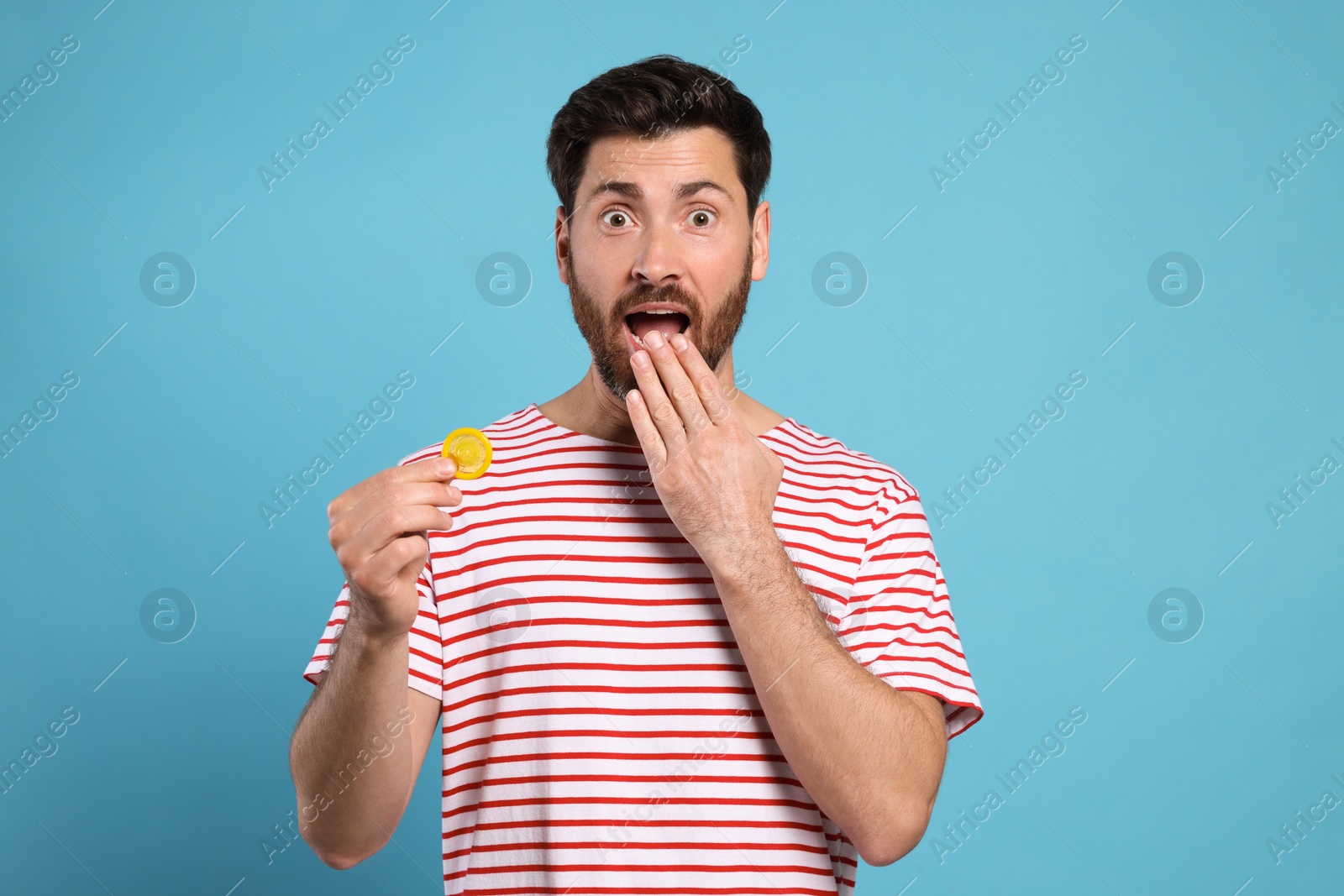 Photo of Emotional man holding condom on light blue background. Safe sex