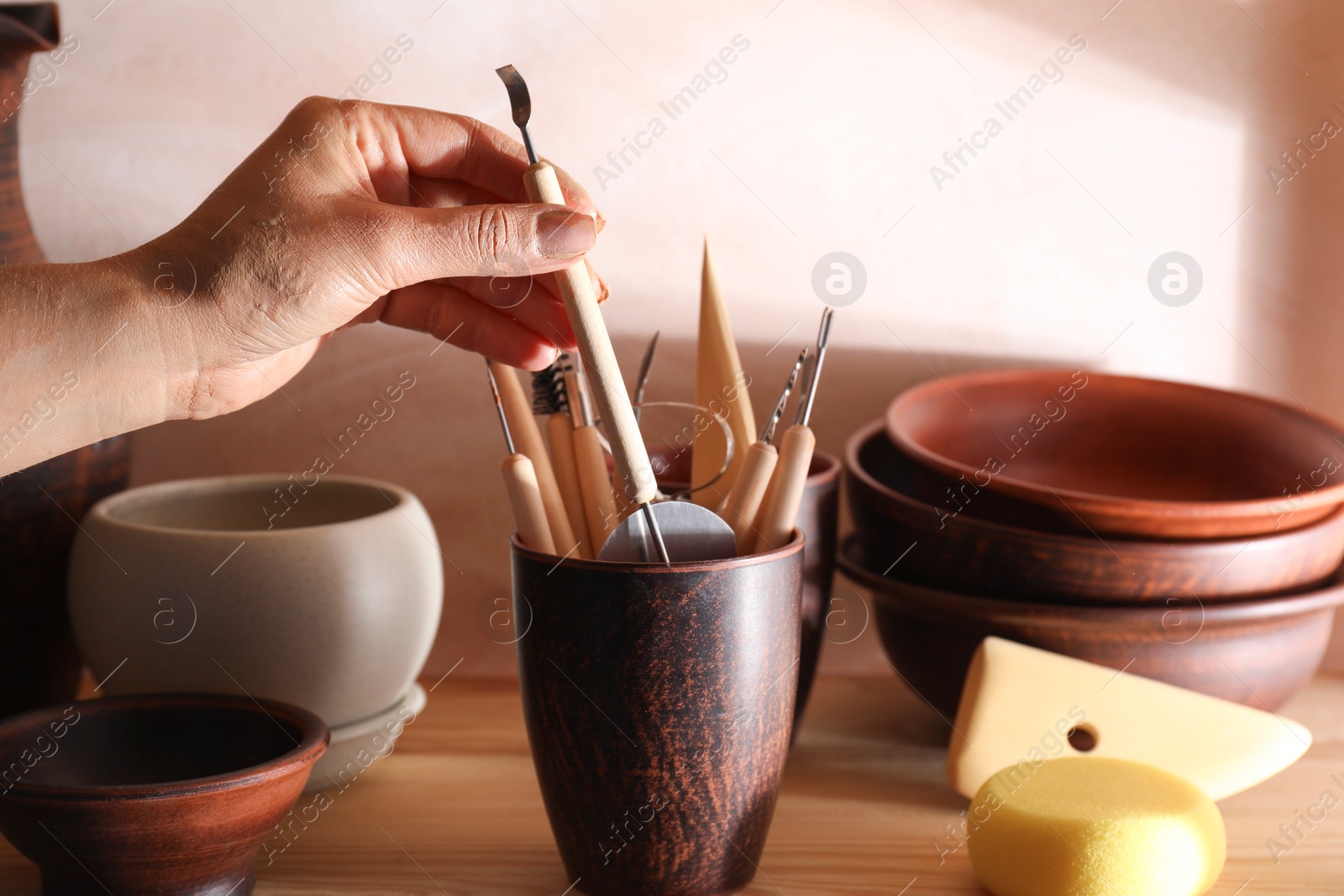 Photo of Woman taking clay crafting tool from cup in workshop, closeup