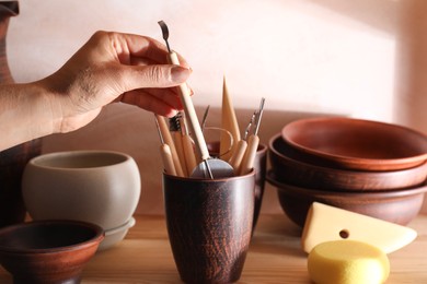 Woman taking clay crafting tool from cup in workshop, closeup