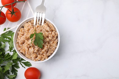 Tasty wheat porridge with parsley and tomatoes in bowl on white table, flat lay. Space for text