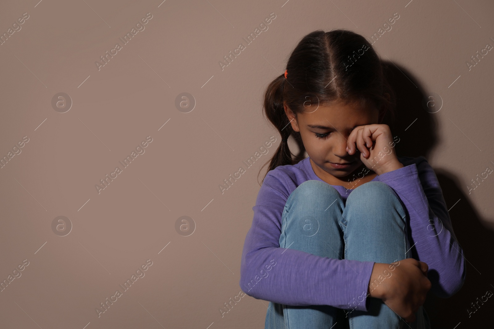 Photo of Crying little girl near beige wall, space for text. Domestic violence concept