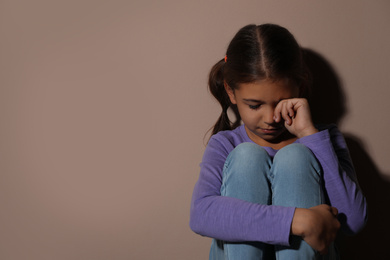 Crying little girl near beige wall, space for text. Domestic violence concept