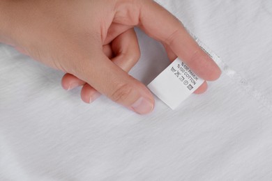 Photo of Woman holding clothing label on white garment, top view