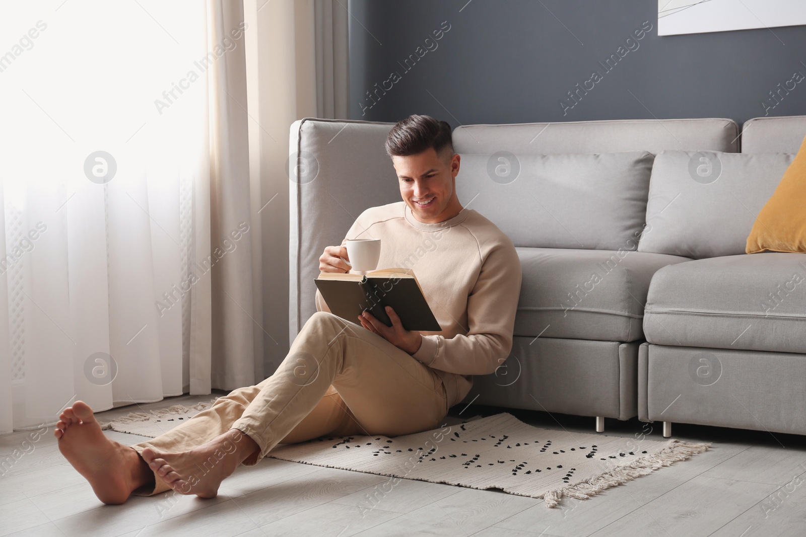 Photo of Man with cup of hot drink reading book at home. Floor heating concept