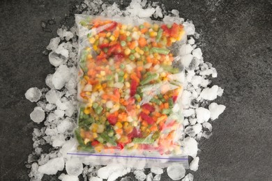Photo of Zip bag with different frozen vegetables and ice on grey table, top view