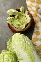 Photo of Fresh ripe Chinese cabbages and green leaves in bowl on gray table, flat lay