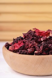 Photo of Dry hibiscus tea in bowl on white table, closeup