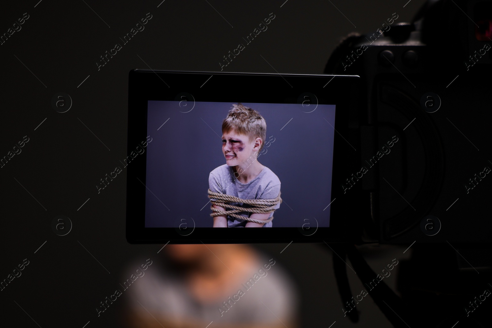 Photo of Little boy with bruises tied up and taken hostage on dark background, view through camera screen