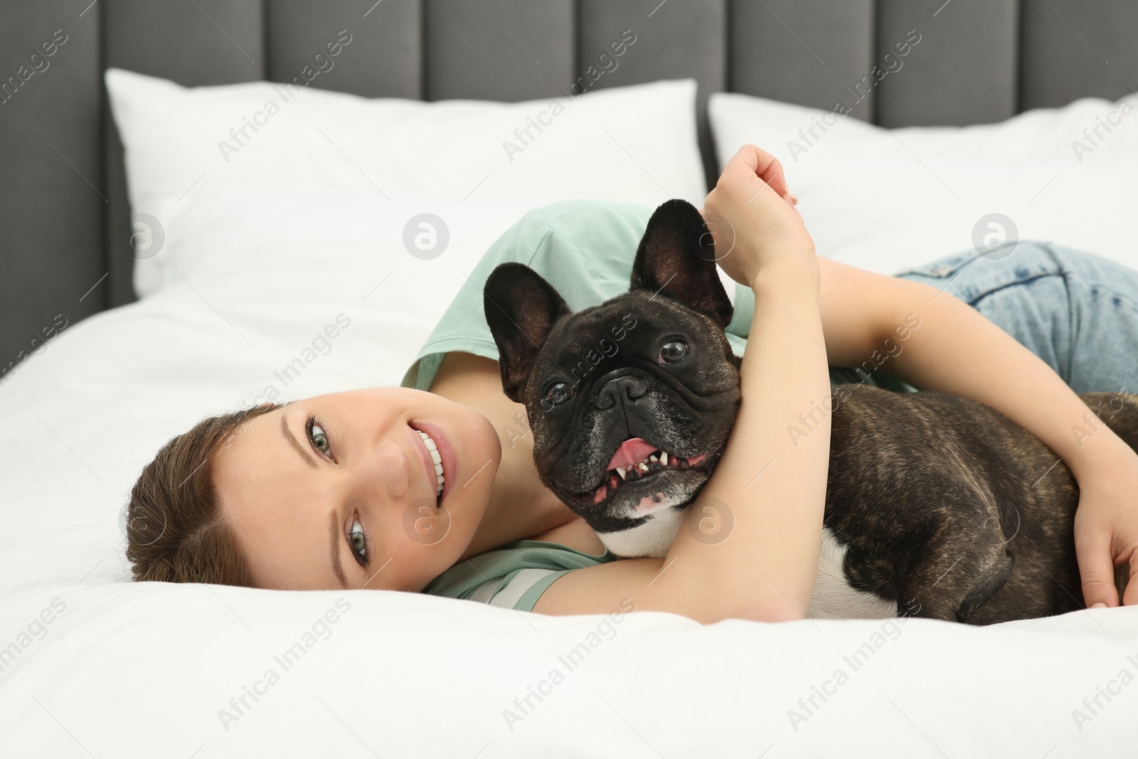 Photo of Happy woman hugging with cute French Bulldog on bed in room