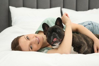 Happy woman hugging with cute French Bulldog on bed in room