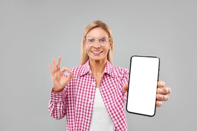 Photo of Happy woman holding smartphone with blank screen and showing OK gesture on grey background