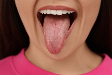 Photo of Happy young woman showing her tongue on pink background, closeup