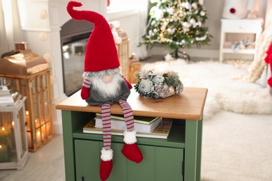 Photo of Cute Christmas gnome on wooden table in room with festive decorations