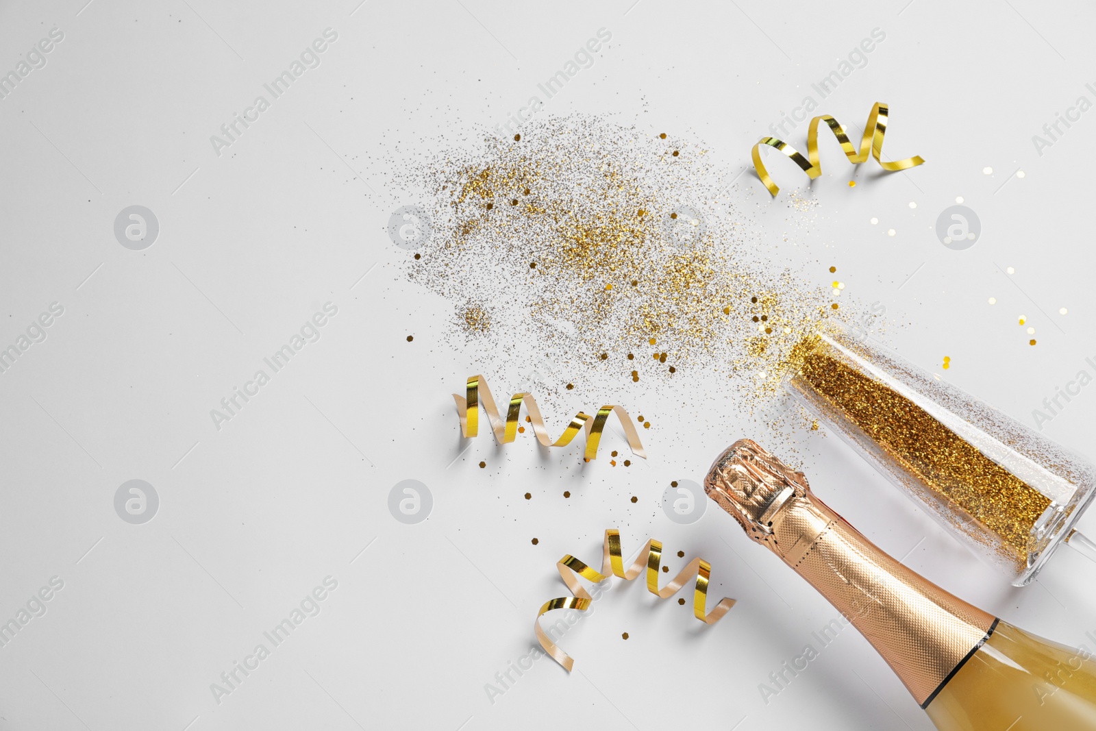 Photo of Bottle of champagne, glass with gold glitter and space for text on white background, top view. Hilarious celebration