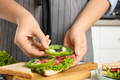 Photo of Woman making sandwich with green bell pepper and sausage at table, closeup