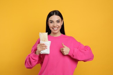 Photo of Happy young woman with delicious shawarma on yellow background
