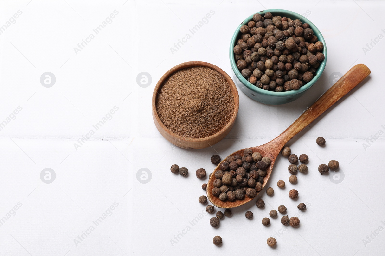 Photo of Ground and whole allspice berries (Jamaica pepper) on white tiled table, flat lay. Space for text