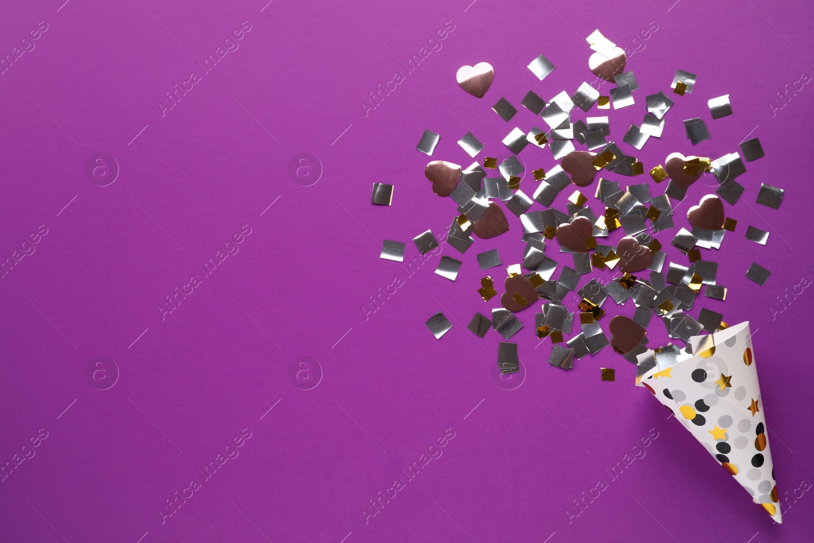 Photo of Golden and silver confetti with party cracker on purple background, top view. Space for text