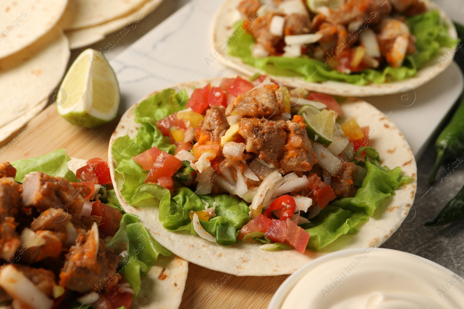 Photo of Delicious tacos with vegetables and meat on table, closeup