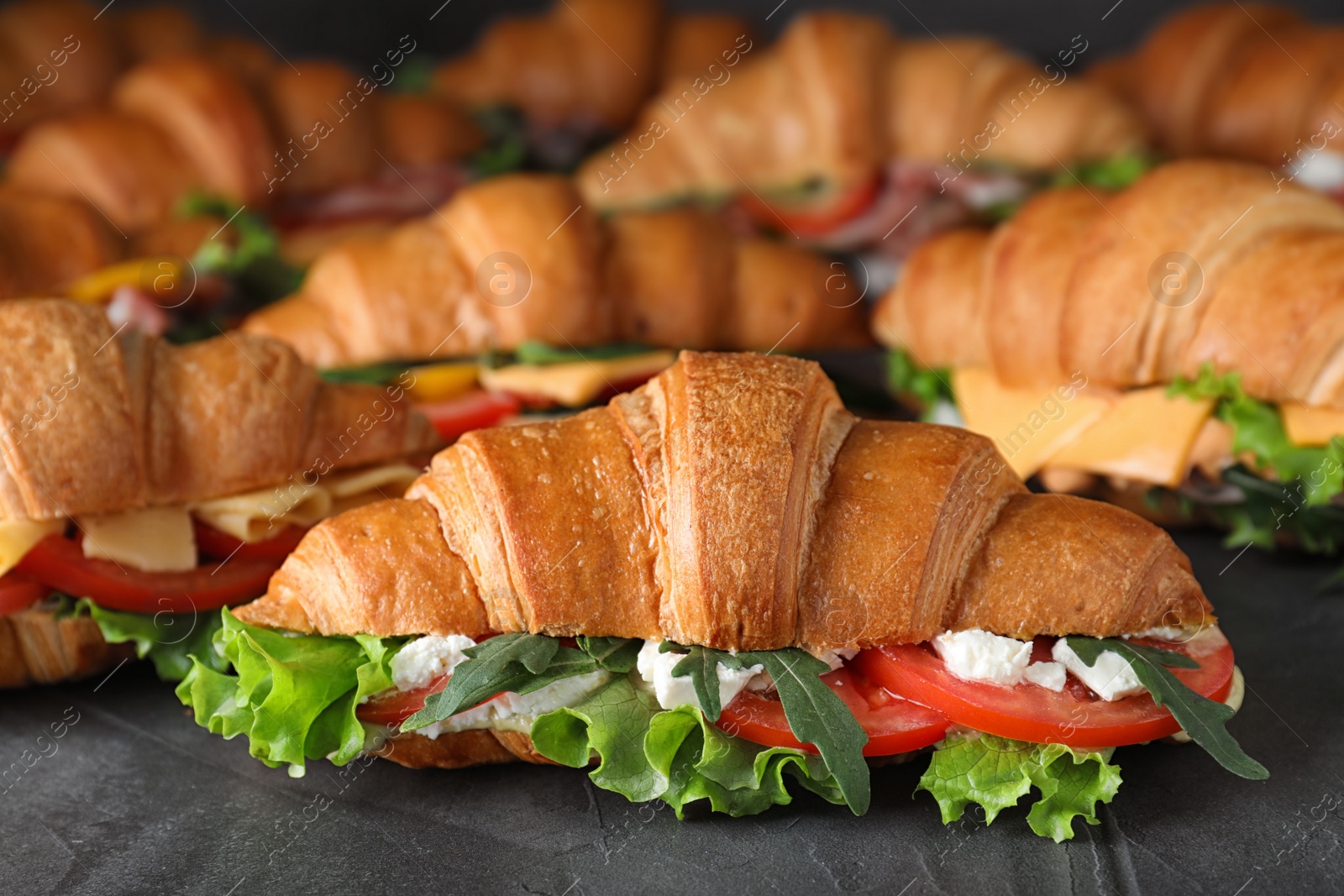 Photo of Bunch of tasty croissant sandwiches on grey table