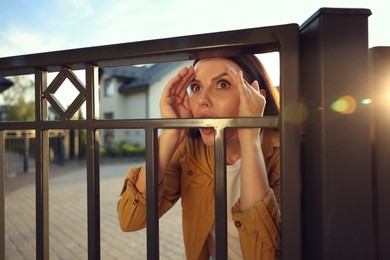 Concept of private life. Curious woman spying on neighbours over fence outdoors