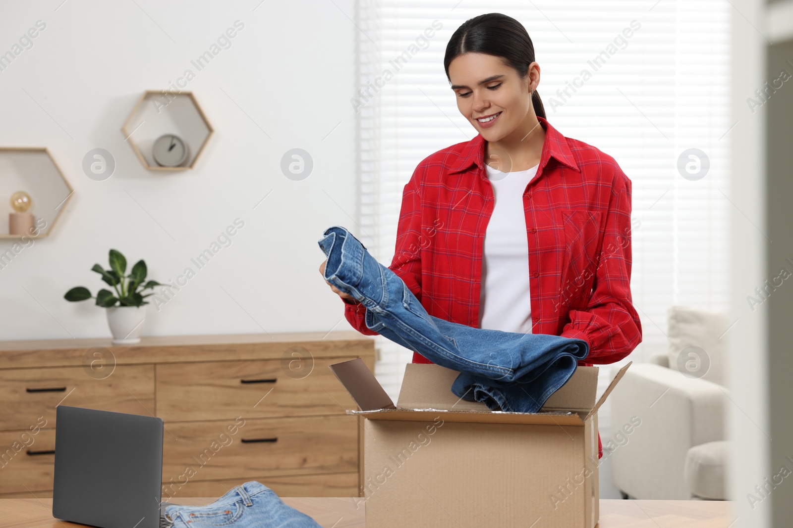 Photo of Young woman with just unpacked new jeans at wooden table indoors. Online shopping