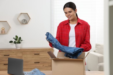 Young woman with just unpacked new jeans at wooden table indoors. Online shopping