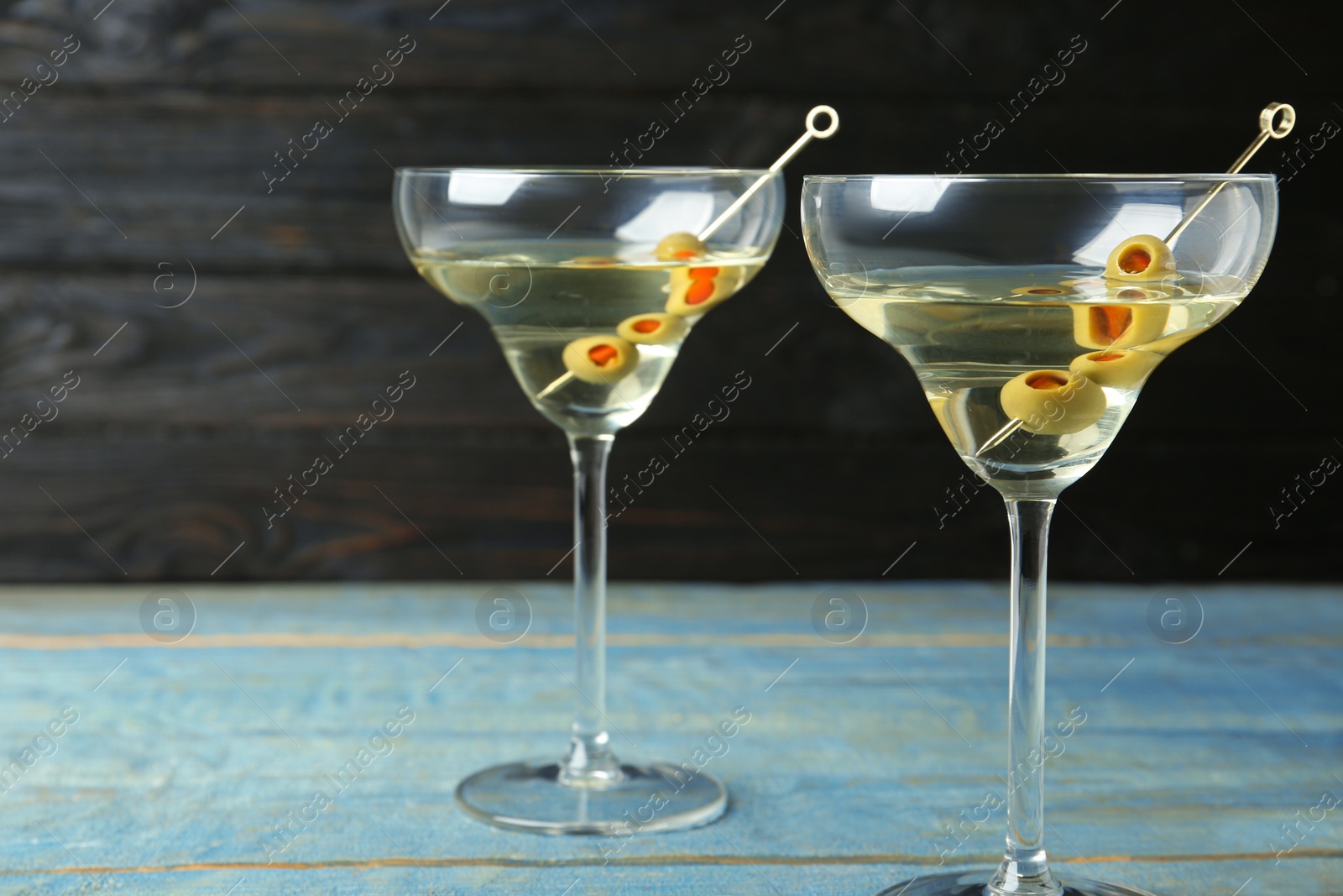 Photo of Glasses of Classic Dry Martini with olives on light blue wooden table against dark background