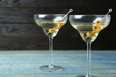 Glasses of Classic Dry Martini with olives on light blue wooden table against dark background