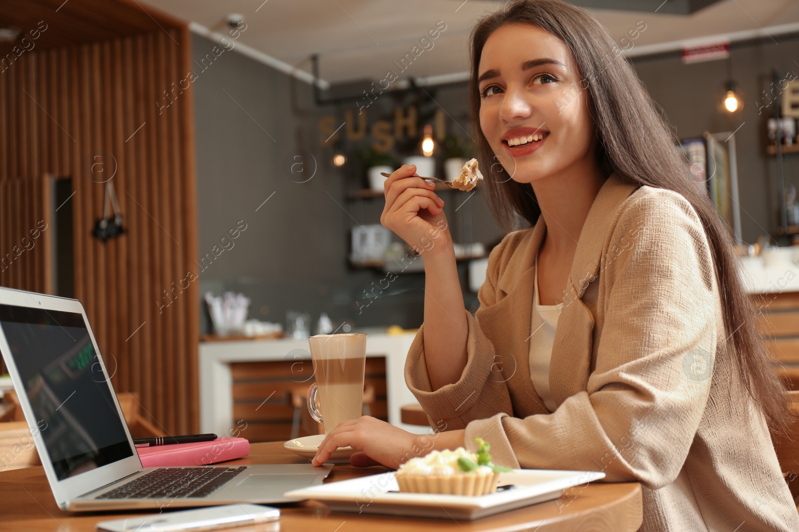 Photo of Young blogger with laptop eating cake in cafe