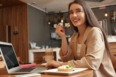 Photo of Young blogger with laptop eating cake in cafe