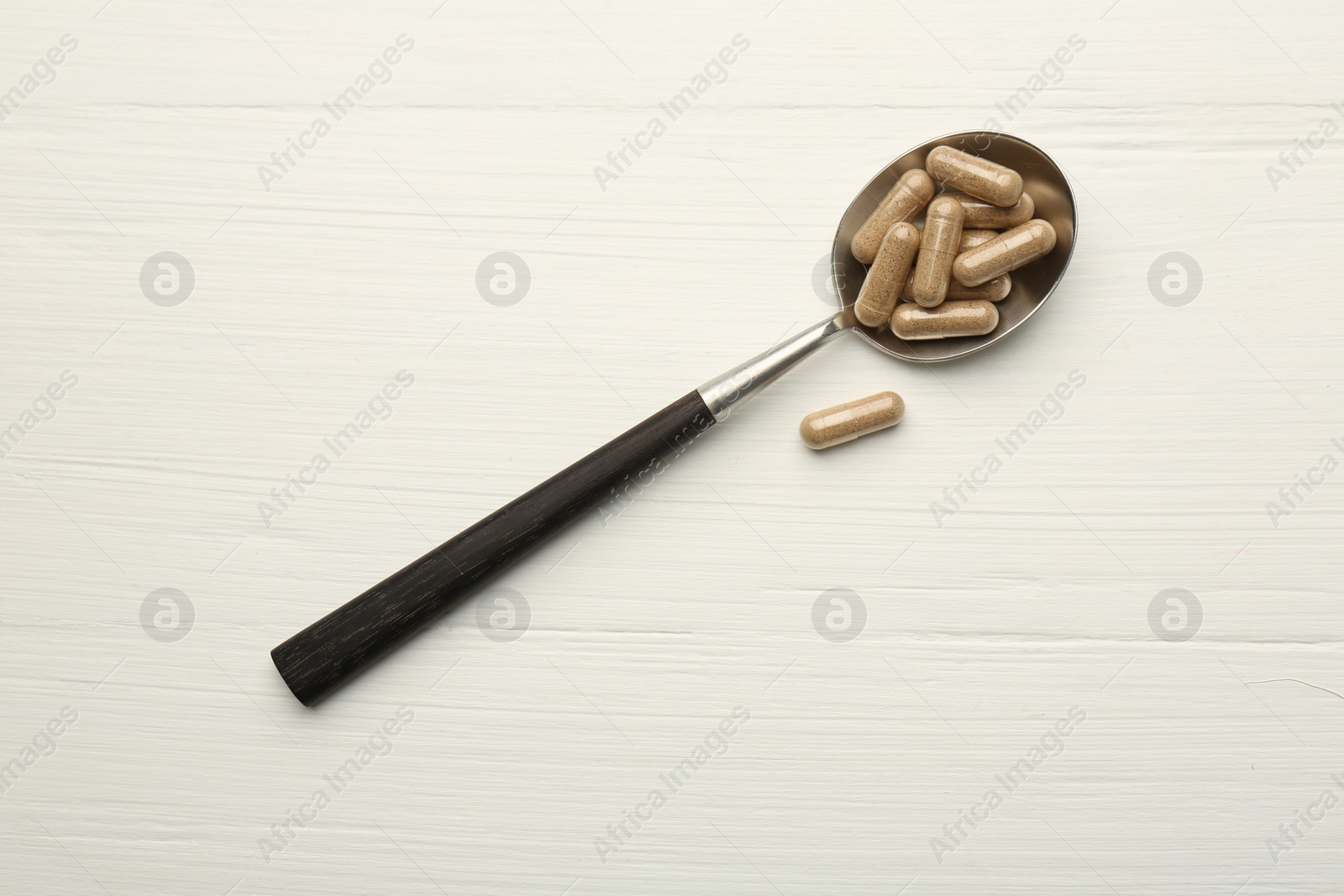 Photo of Vitamin capsules in spoon on white wooden table, top view