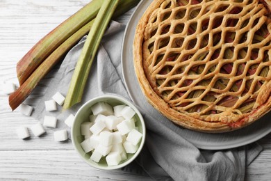 Freshly baked rhubarb pie, stalks and sugar cubes on light wooden table, flat lay