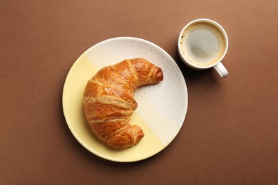 Delicious fresh croissant and cup of coffee on brown table, flat lay