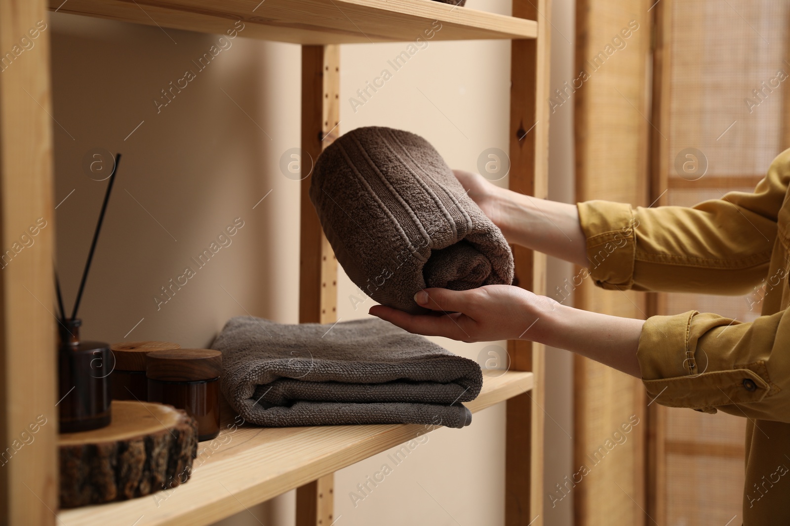 Photo of Woman putting rolled towel onto shelf indoors, closeup