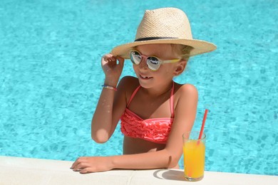 Photo of Cute little girl with glass of juice in swimming pool on sunny day