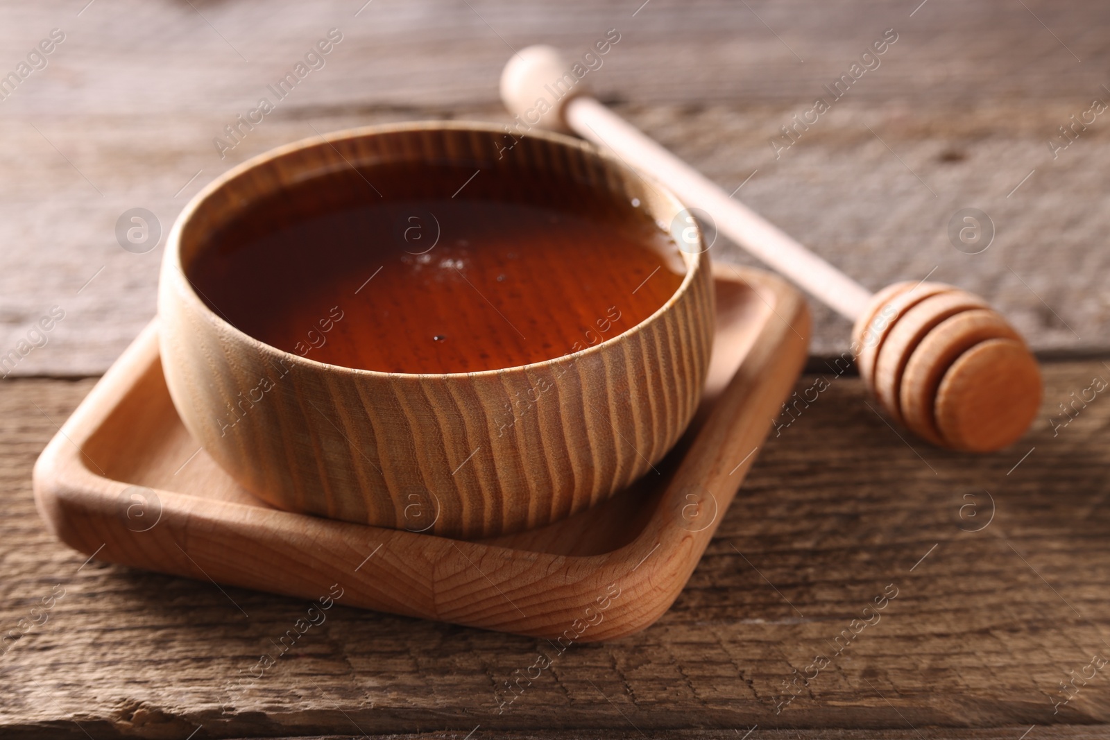 Photo of Delicious honey in bowl and dipper on wooden table, closeup