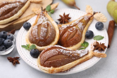Delicious pears baked in puff pastry with powdered sugar served on light grey table, closeup
