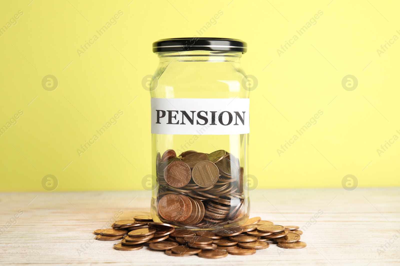 Photo of Glass jar with label PENSION and coins on table against yellow background