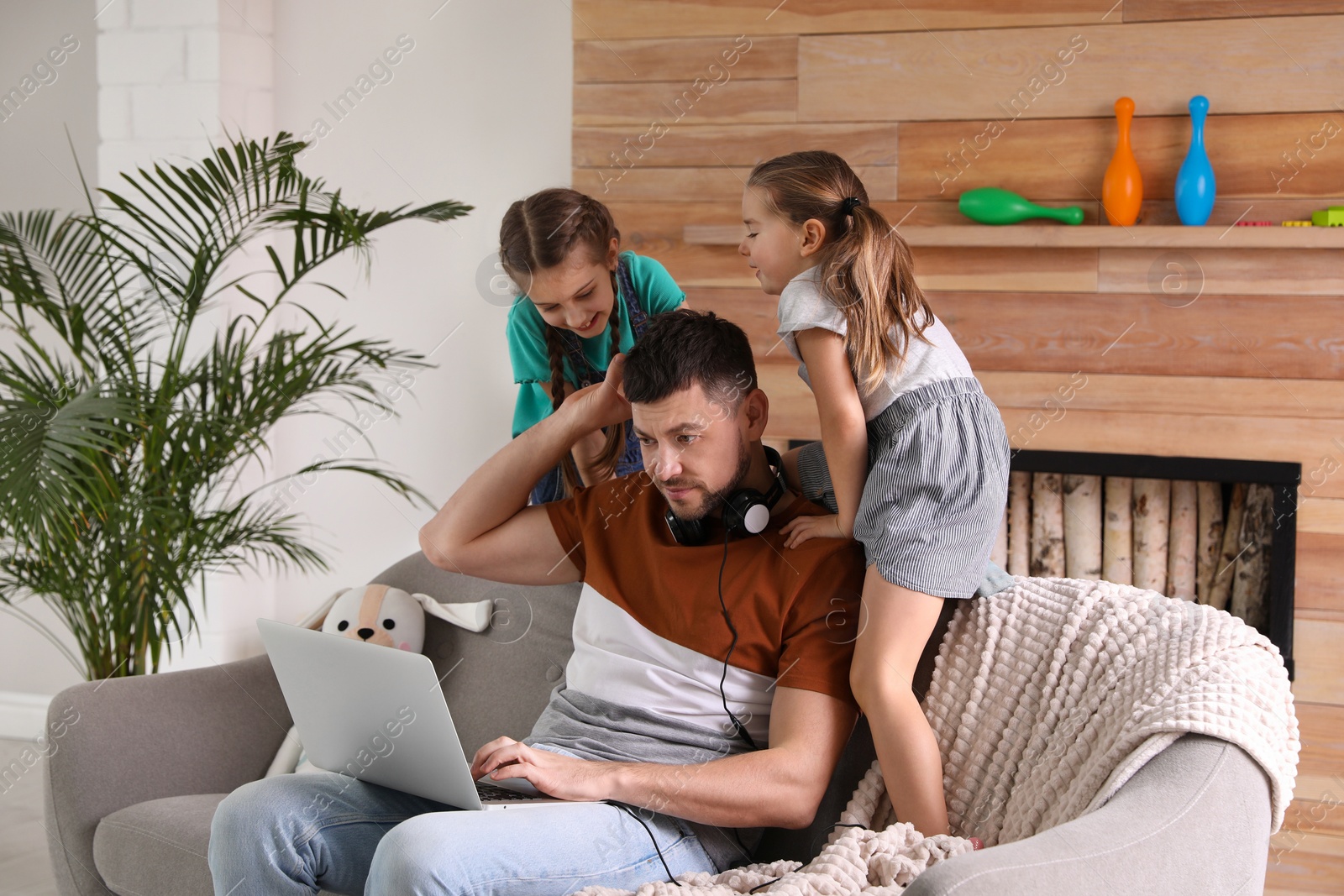 Photo of Children disturbing stressed man in living room. Working from home during quarantine