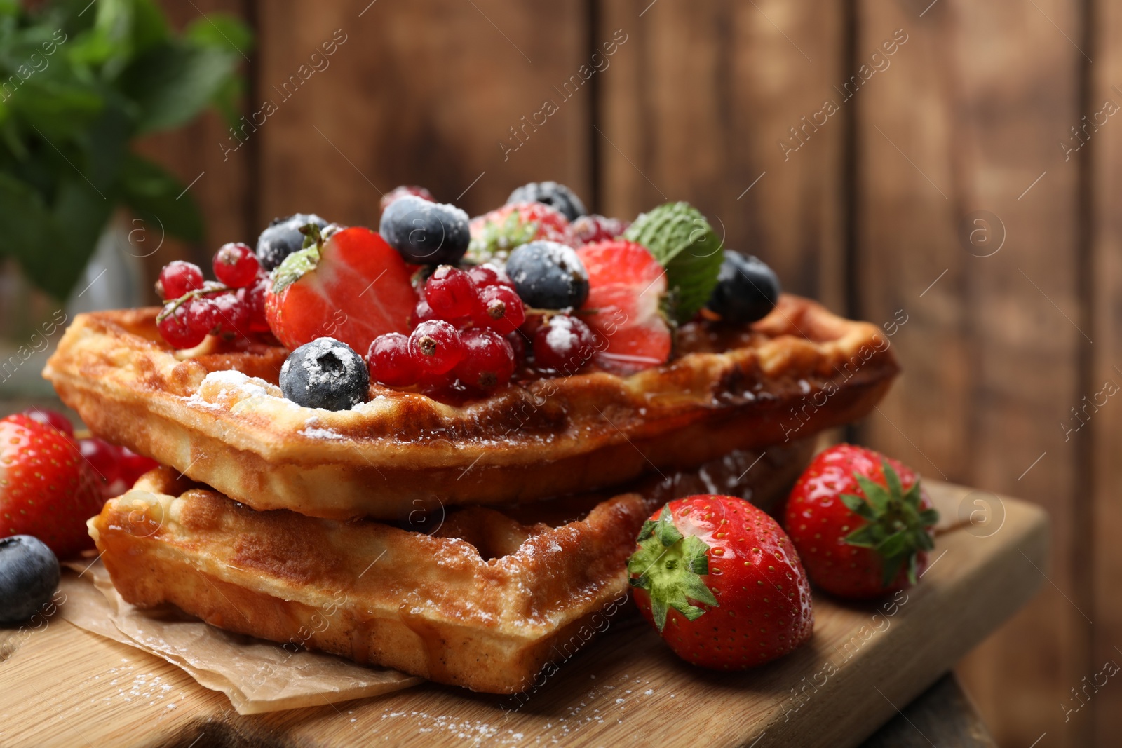 Photo of Delicious Belgian waffles, berries and powdered sugar on wooden board, closeup
